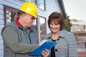 Contractor wearing hardhat reviewing notes on clipboard with a homeowner.