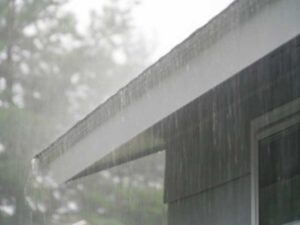 Heavy rain downpour on corner of roof without gutters.