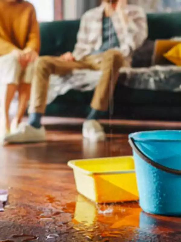 Living room with hardwood floors showing buckets collecting water from a roof leak.